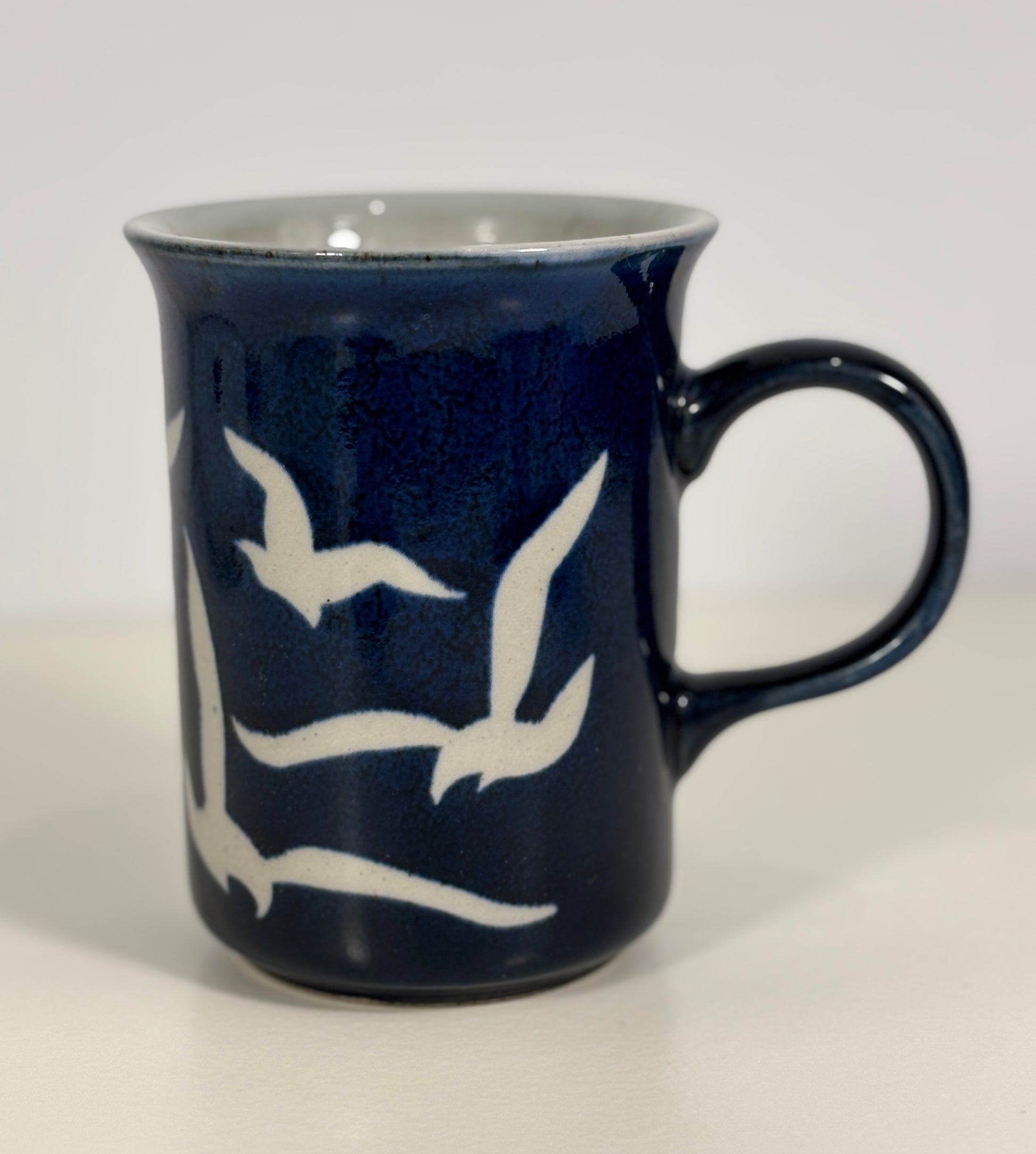 Navy blue mug with white bird designs on a light gray background
