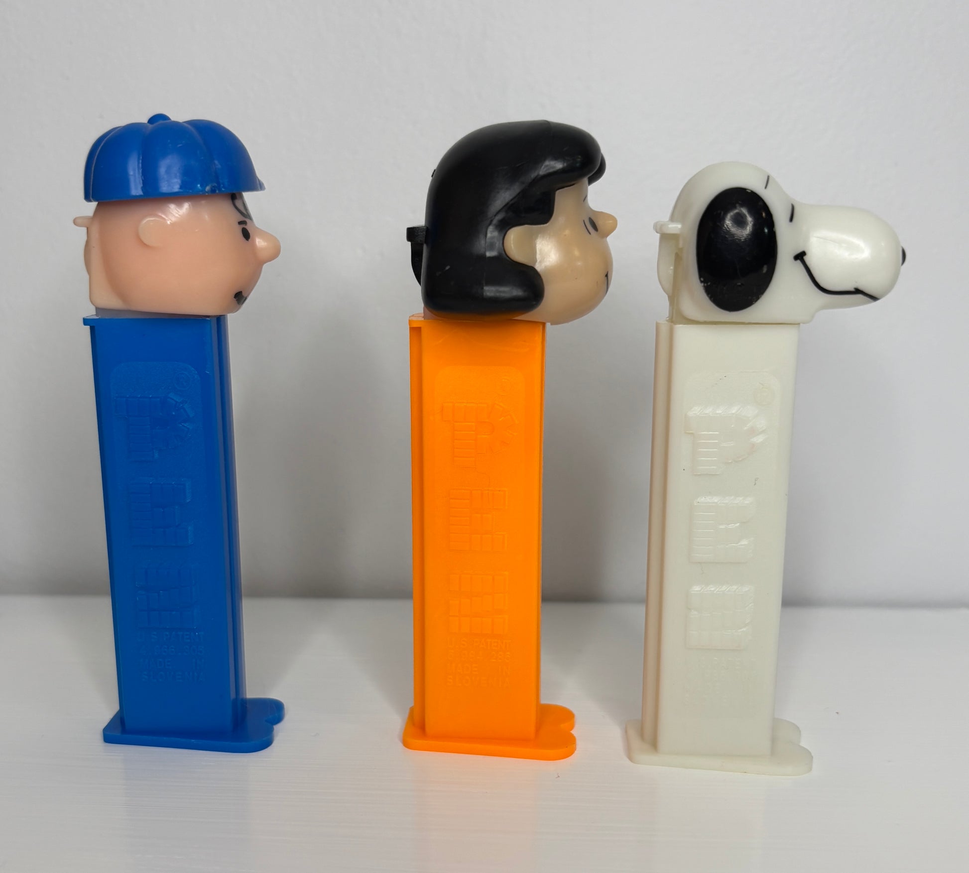 Three Pez dispensers shaped like a person, a dog, and a person with a blue cap on a white background.