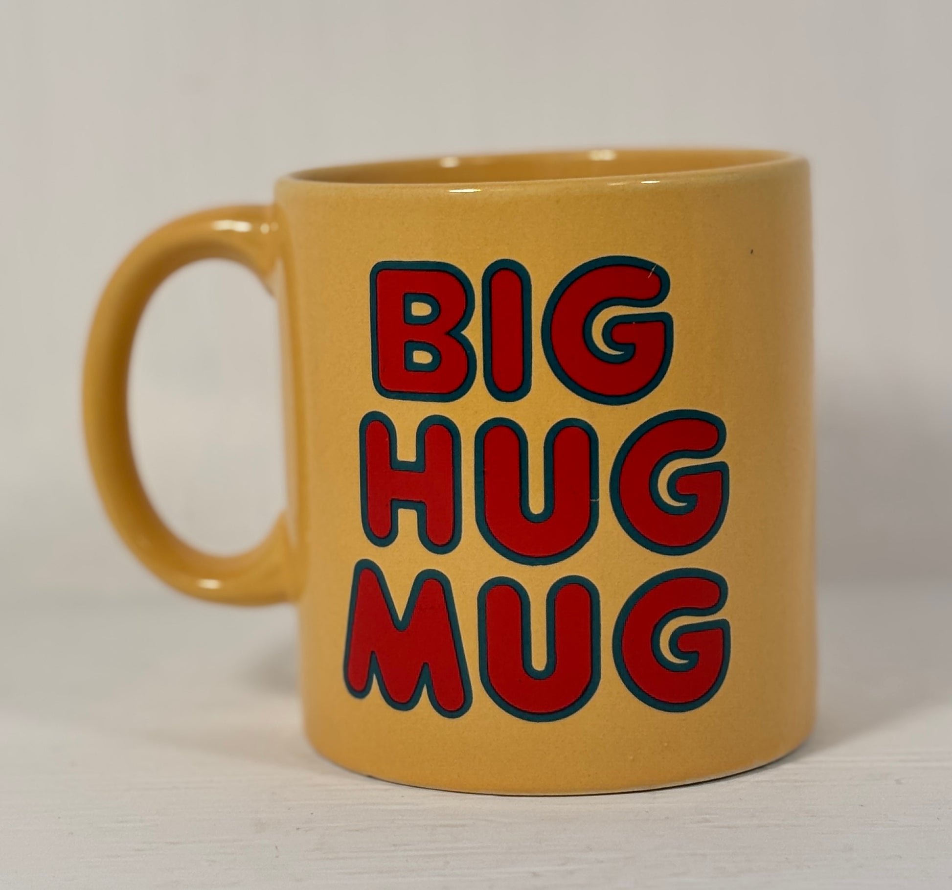 Beige mug with 'BIG HUG MUG' text in red and black on a white background
