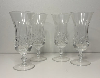 Four clear glass goblets with intricate designs on a white surface and gray background