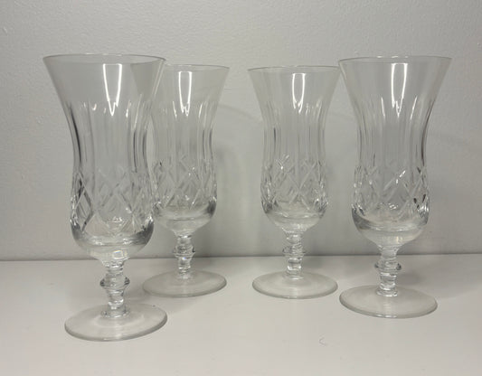 Four clear glass goblets with intricate designs on a white surface and gray background