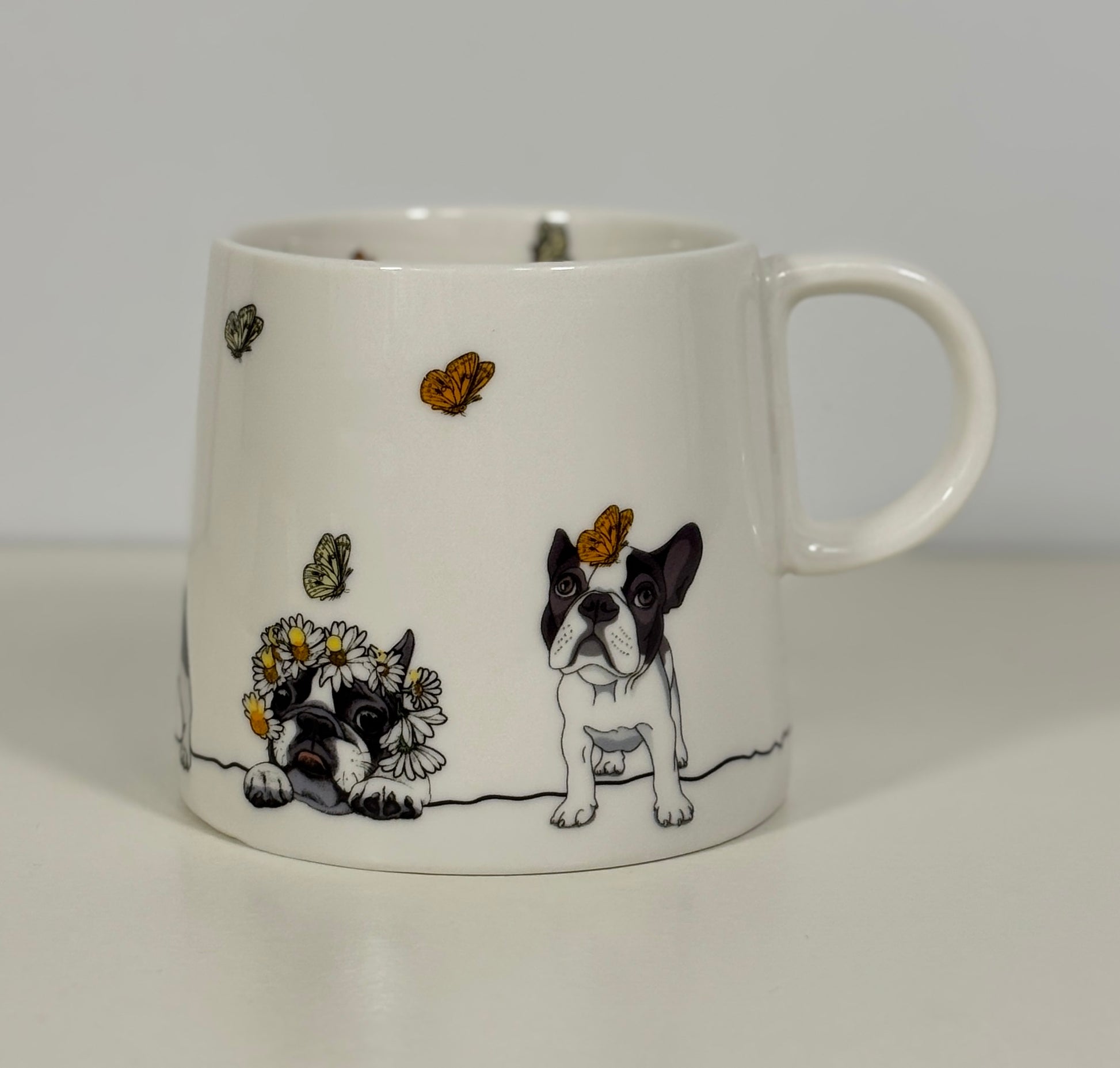 White mug with a design of a black and white dog, butterflies, and flowers on a plain background