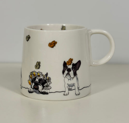 White mug with a design of a black and white dog, butterflies, and flowers on a plain background