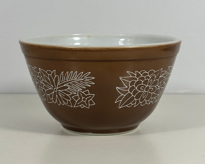 A brown mixing bowl with a white interior and white line-art floral pattern on the exterior, set against a plain light gray background.