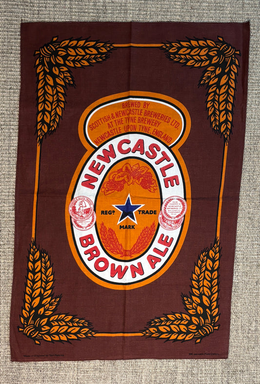 Newcastle Brown Ale logo on a brown background with wheat designs