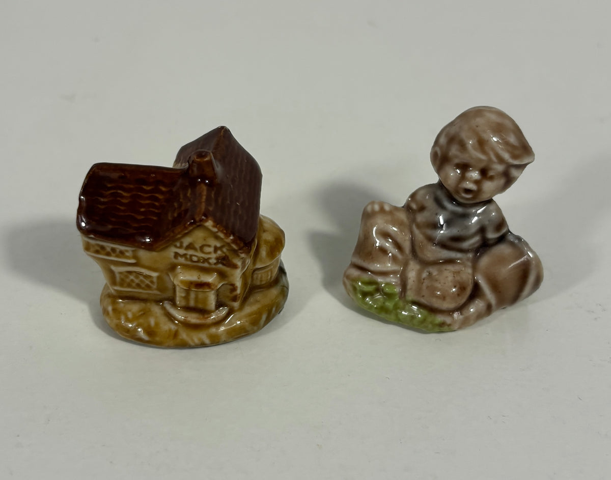 Two small vintage ceramic figurines on a light gray background: a brown house with a dark brown roof and the words 'JACK MOON' on the side, and a seated brown figure with a dark head and green base.