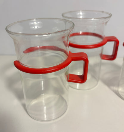 Clear glass beakers with bright red silicone handle grips, shown on a white surface with a white background.