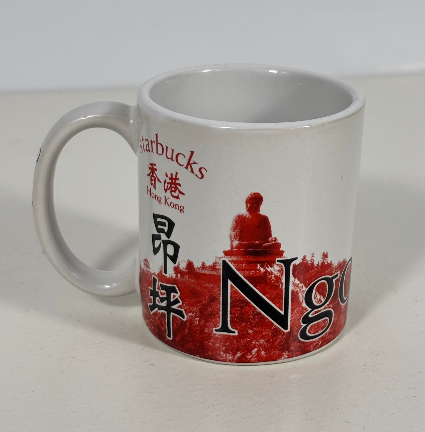 A white ceramic Starbucks coffee mug featuring a red and black graphic design with Chinese characters and a seated figure on a red textured background.