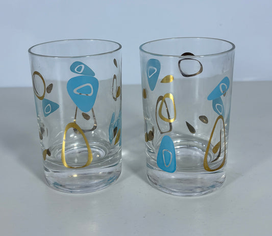 Two clear glass tumblers with a mid-century modern abstract pattern in light blue, gold, and dark brown on a light gray background.