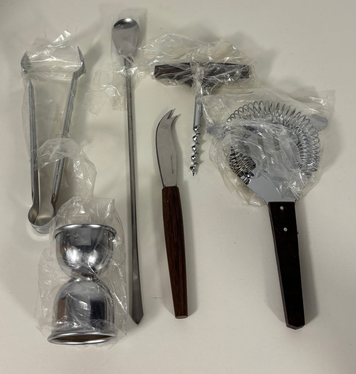 Set of bar tools including a jigger, strainer, and other utensils on a white background.