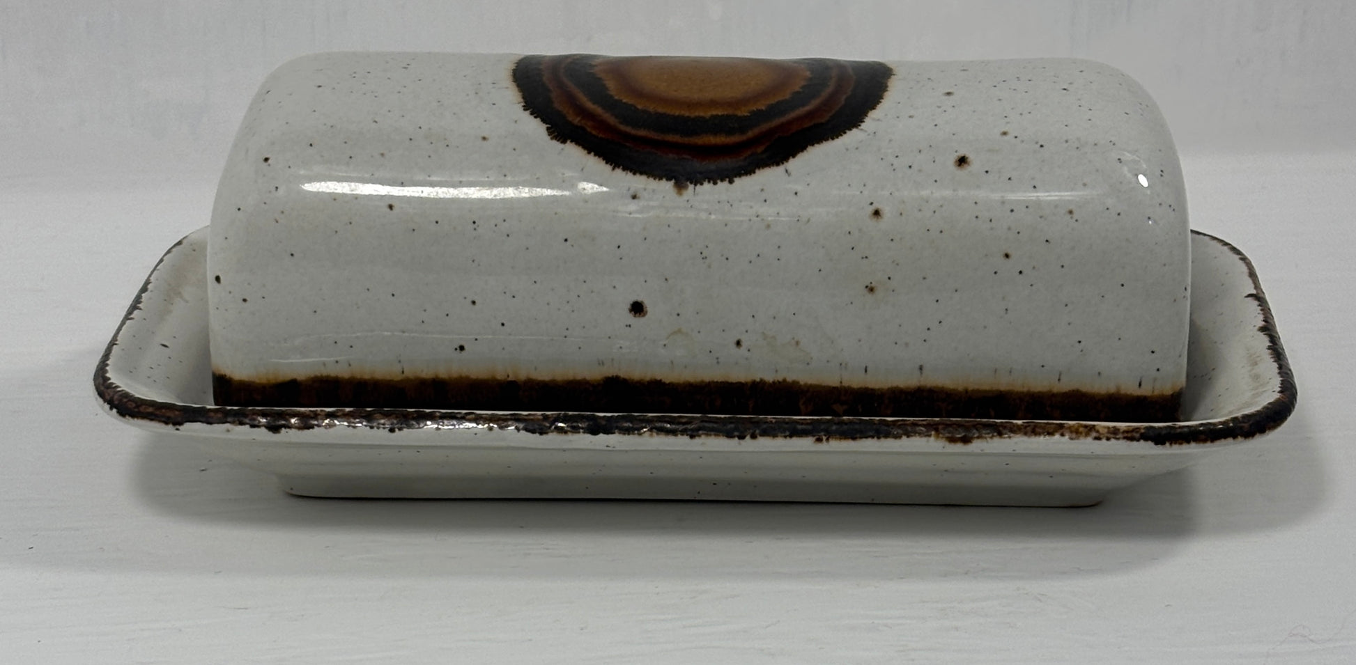 White ceramic butter dish with brown speckles on a white background