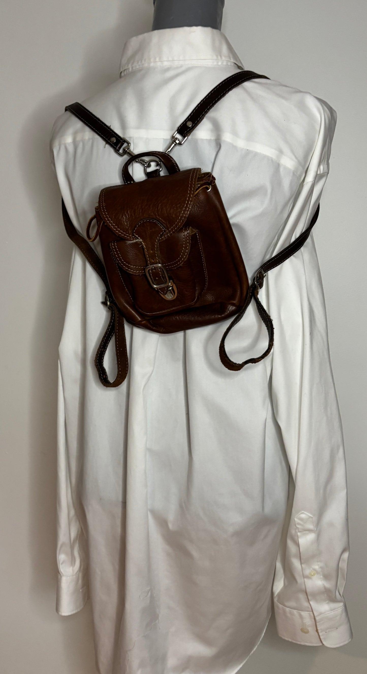 Brown leather backpack on a white shirt against a gray background