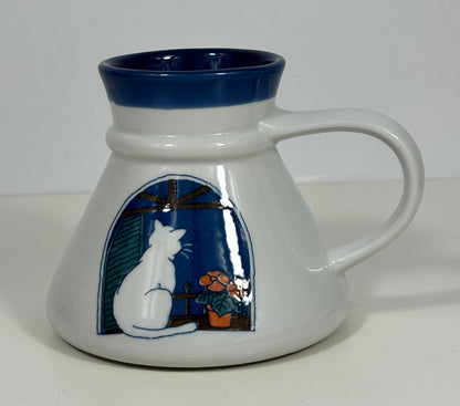 A white ceramic mug with a dark blue interior and handle, featuring a hand-painted illustration of a white cat sitting by a window with flowers.