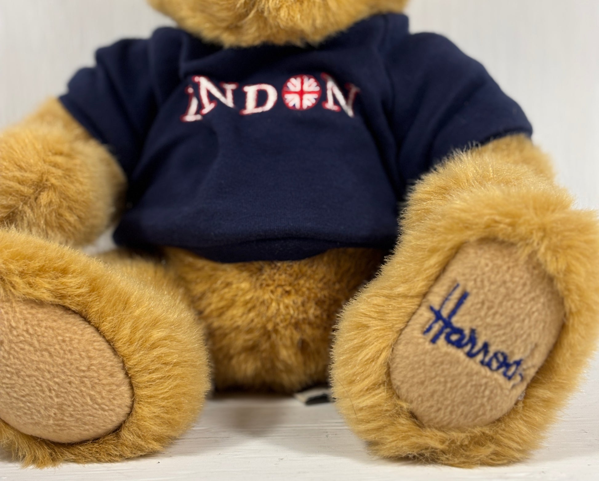 Teddy bear wearing a navy blue shirt with 'London' printed on it, sitting on a white surface.