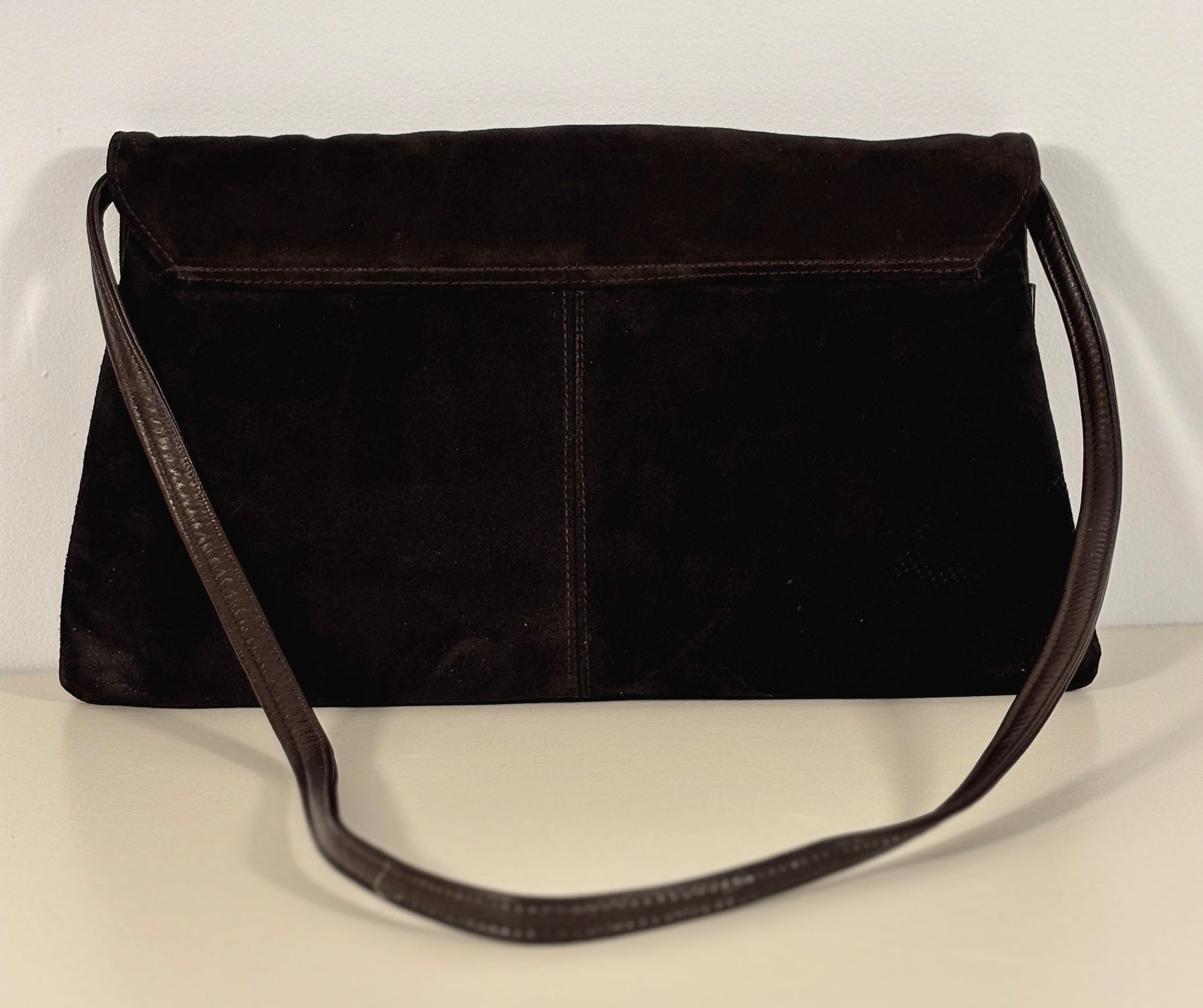 brown suede handbag on a light beige surface with a white background