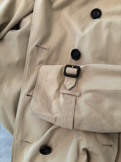 Close-up of a beige trench coat with black buttons and a belt.