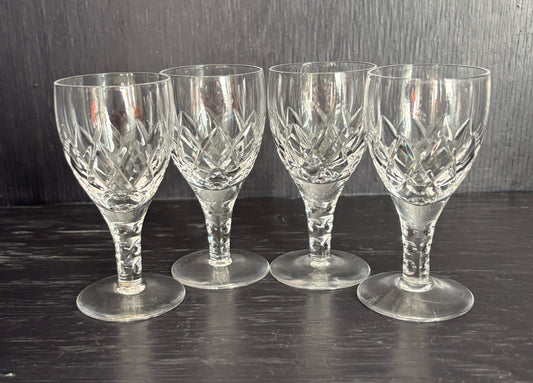 Set of four clear glass sherry glasses on a dark wooden surface