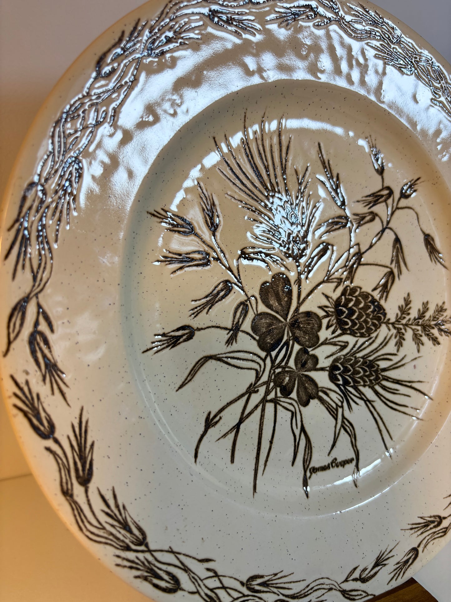 Ceramic plate with black floral and pine cone design on a beige background