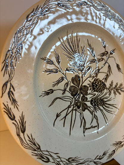 Ceramic plate with black floral and pine cone design on a beige background