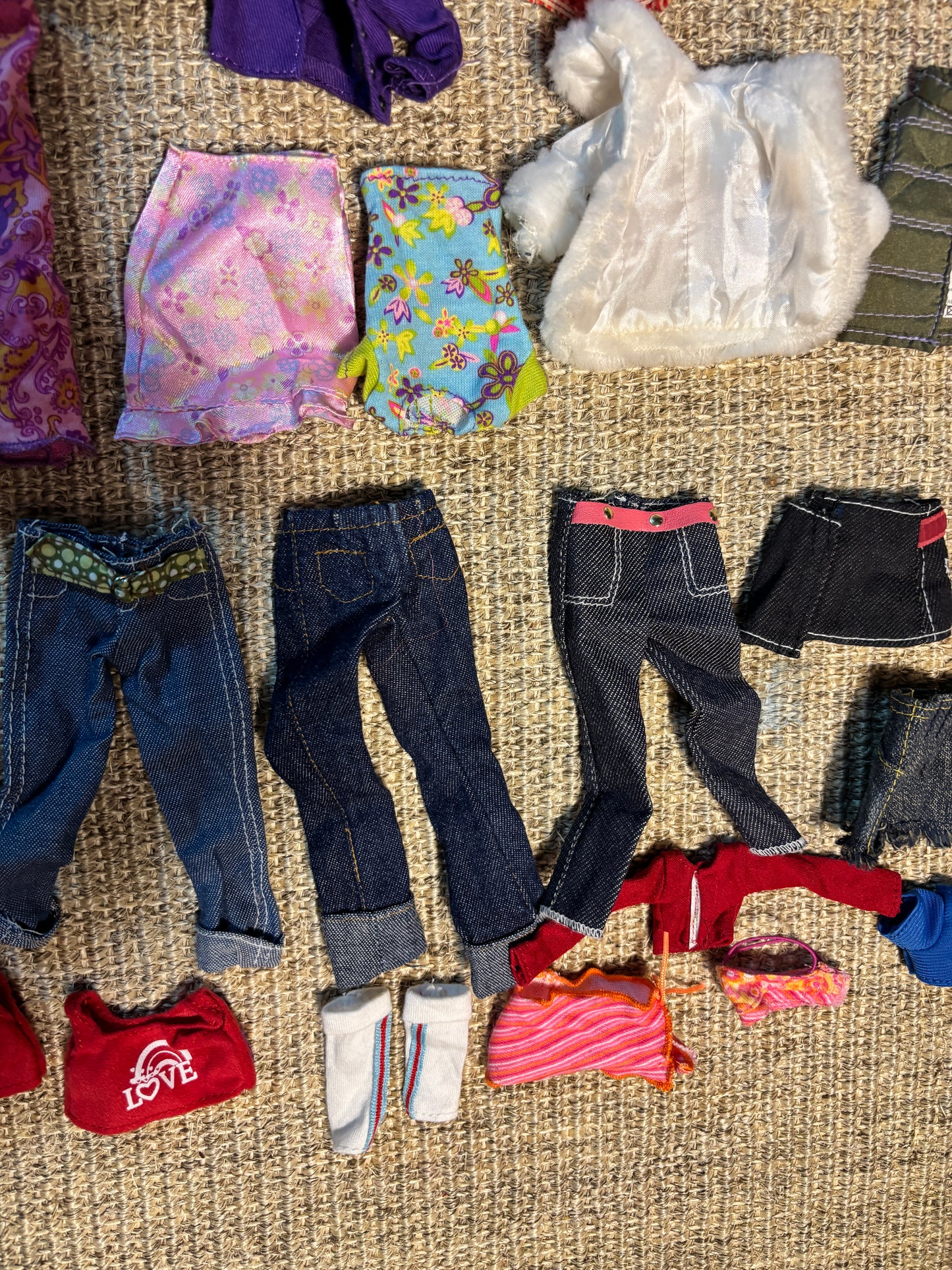 Collection of various doll clothes and accessories on a textured surface