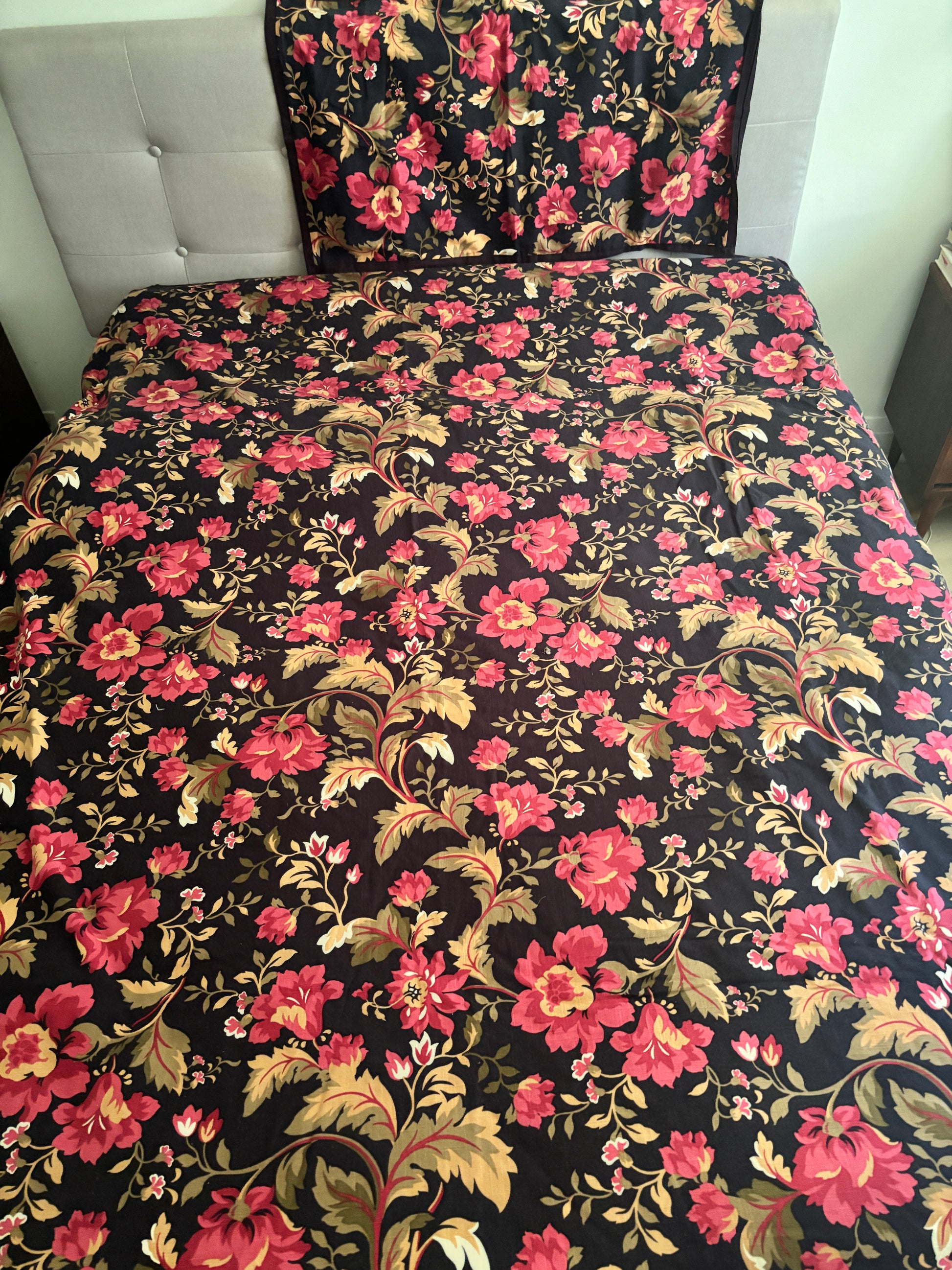 Floral patterned bedspread on a bed with a tufted headboard.