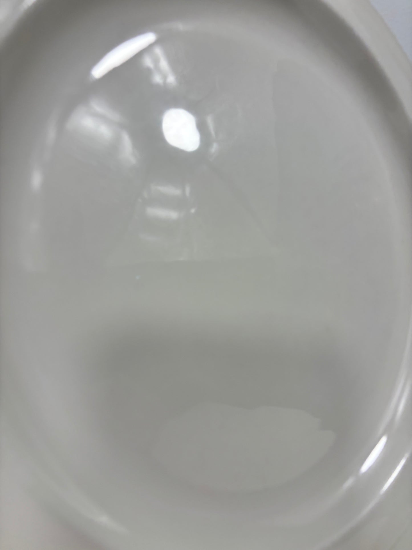 A close-up of a glossy white ceramic plate or dish with a shallow division, showing soft reflections and a slight shadow.