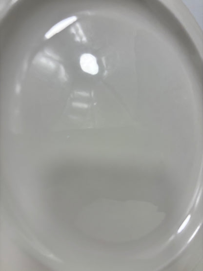 A close-up of a glossy white ceramic plate or dish with a shallow division, showing soft reflections and a slight shadow.