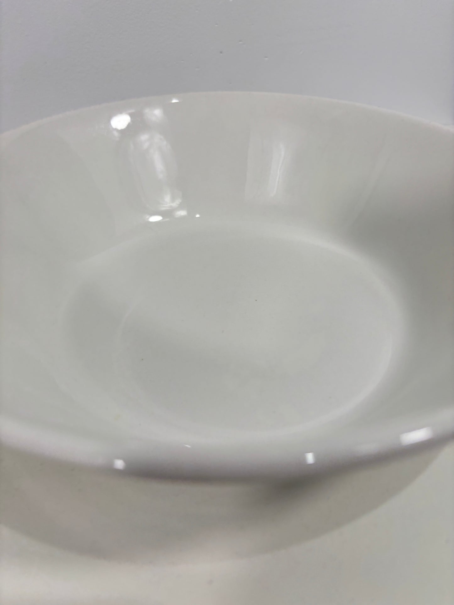 A close-up of a glossy white ceramic bowl or plate against a light gray background.