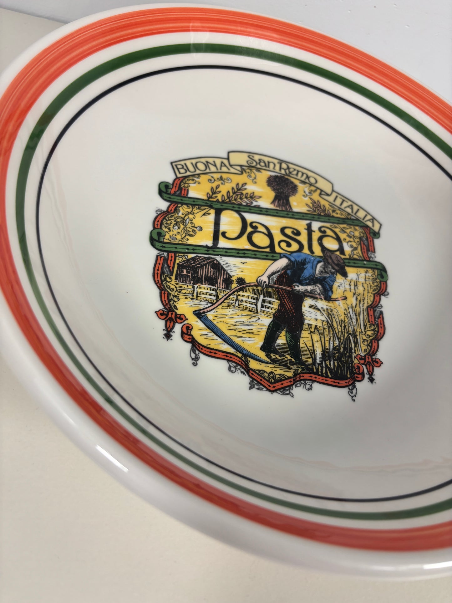 A white ceramic bowl with a colorful central illustration of a pasta maker and the word 'Pasta,' plus orange, green, and black rim stripes.