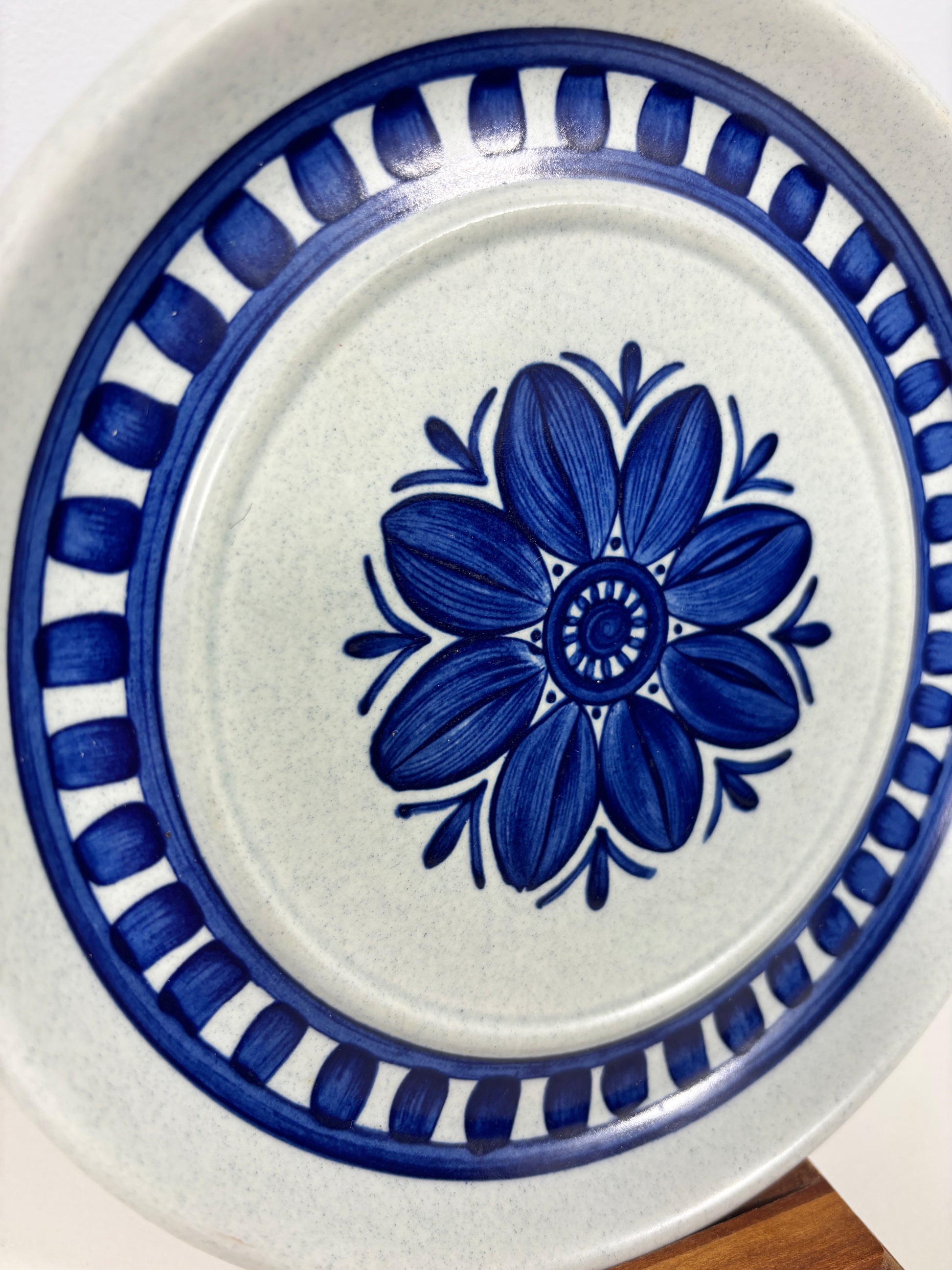 A close-up of a ceramic plate with a white speckled glaze, featuring a central blue floral motif and a blue decorative border.