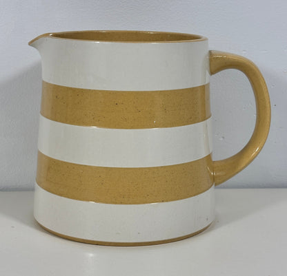 A ceramic pitcher with a glossy finish, featuring alternating horizontal stripes of white and a warm sandy beige, with a matching beige handle and spout.