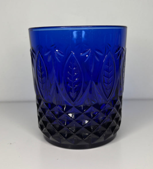 Blue glass tumbler with diamond and leaf patterns on a white background