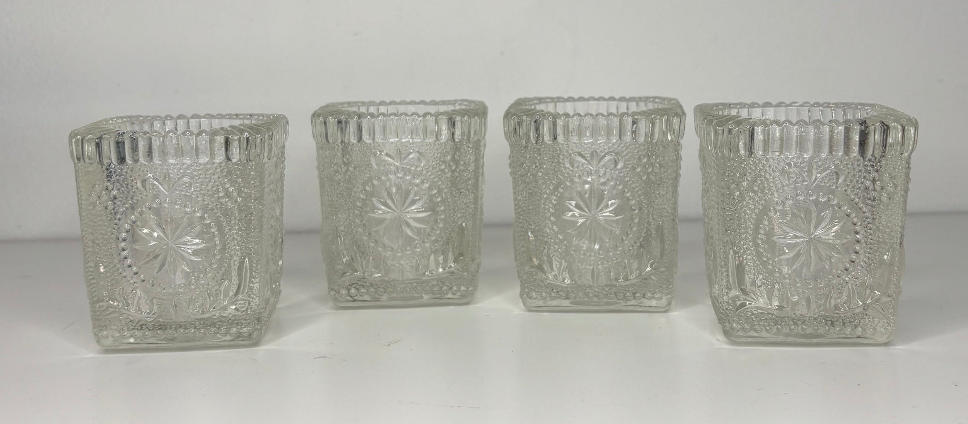 Four clear glass candle holders with textured design on a white background