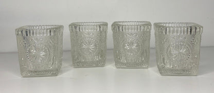 Four clear glass candle holders with textured design on a white background