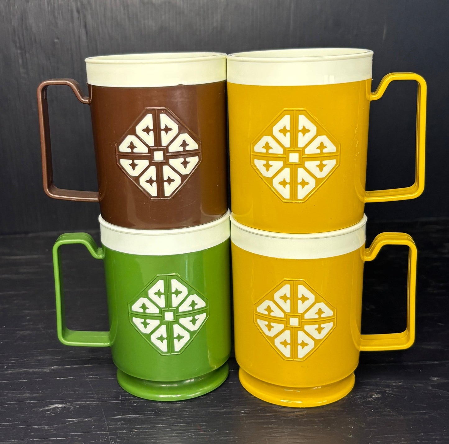 Four stacked mugs in brown, yellow, green, and red with geometric patterns on a dark background.