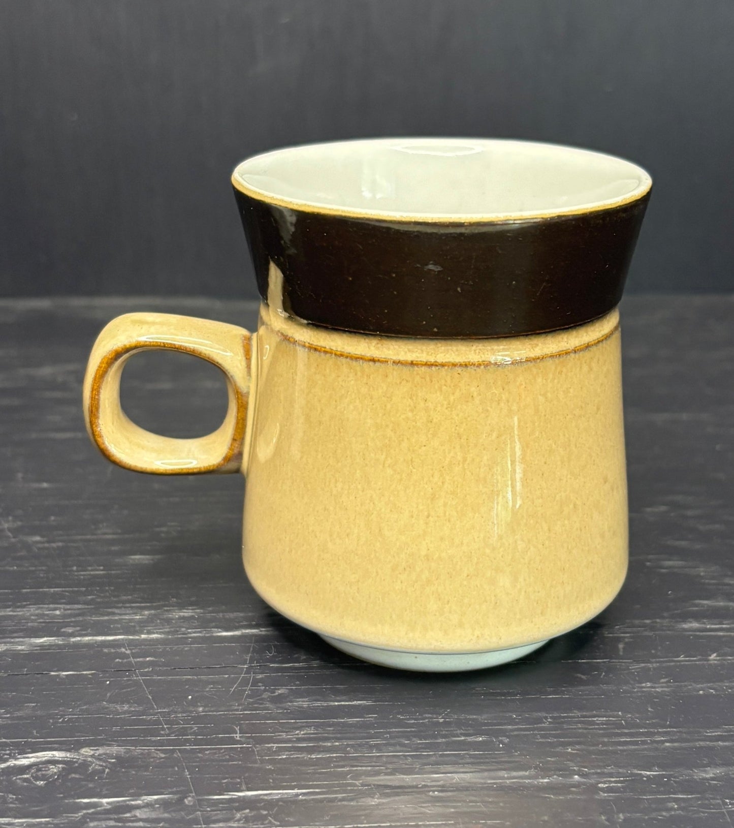Beige ceramic mug with black rim on a dark surface
