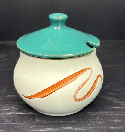 Ceramic jar with teal lid and orange design on a dark surface