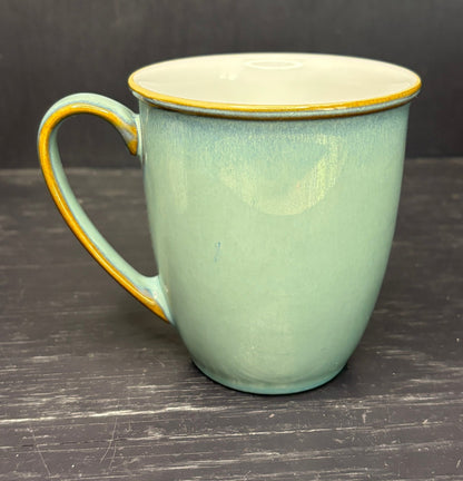 Green ceramic mug with gold rim and handle on a dark wooden surface
