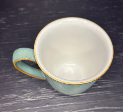 Light blue ceramic mug with gold rim on a dark textured surface