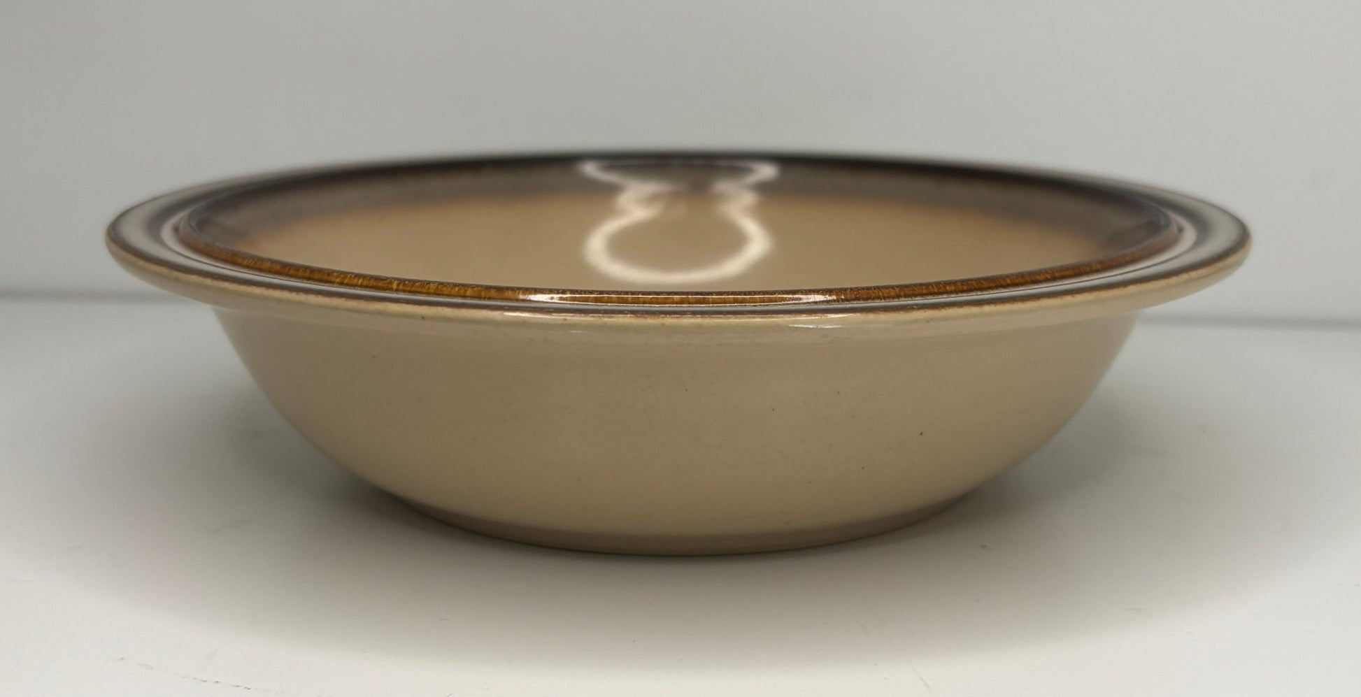 Beige ceramic bowl with brown rim on a white background