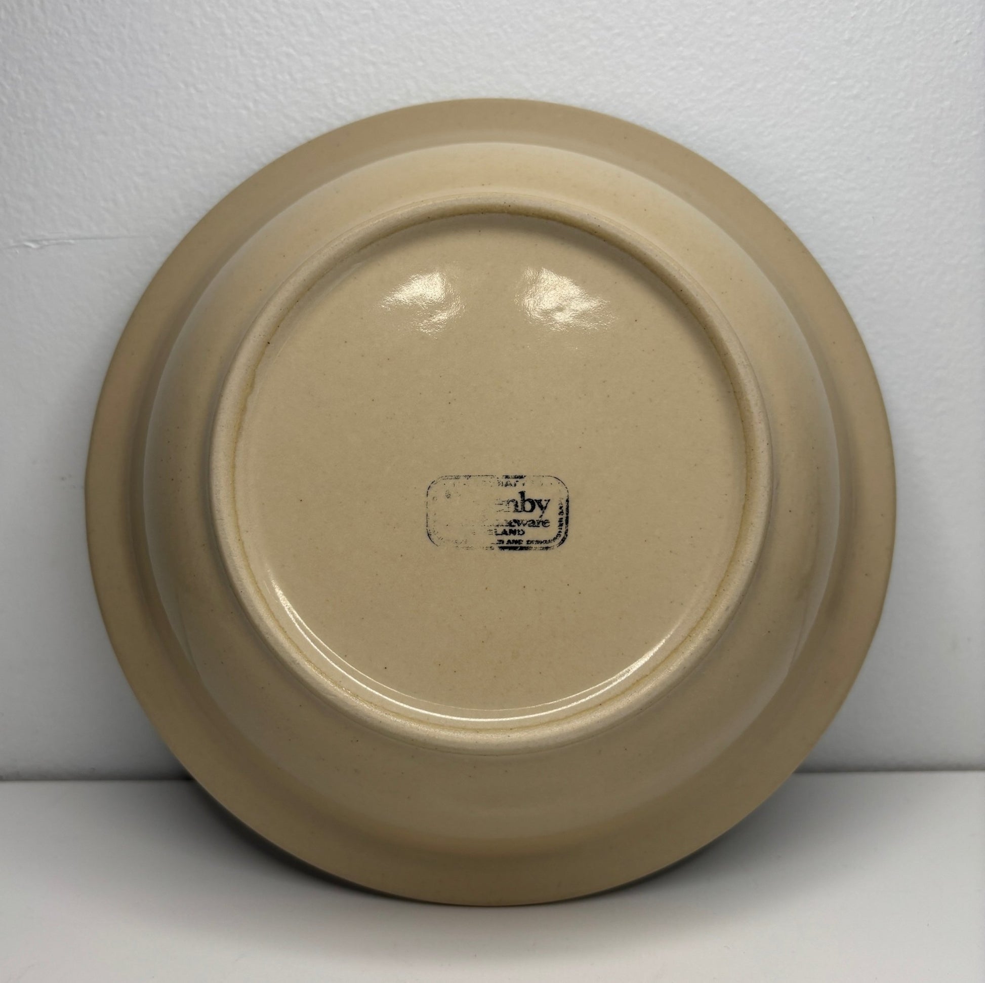 Beige ceramic plate with a visible brand logo on a white background