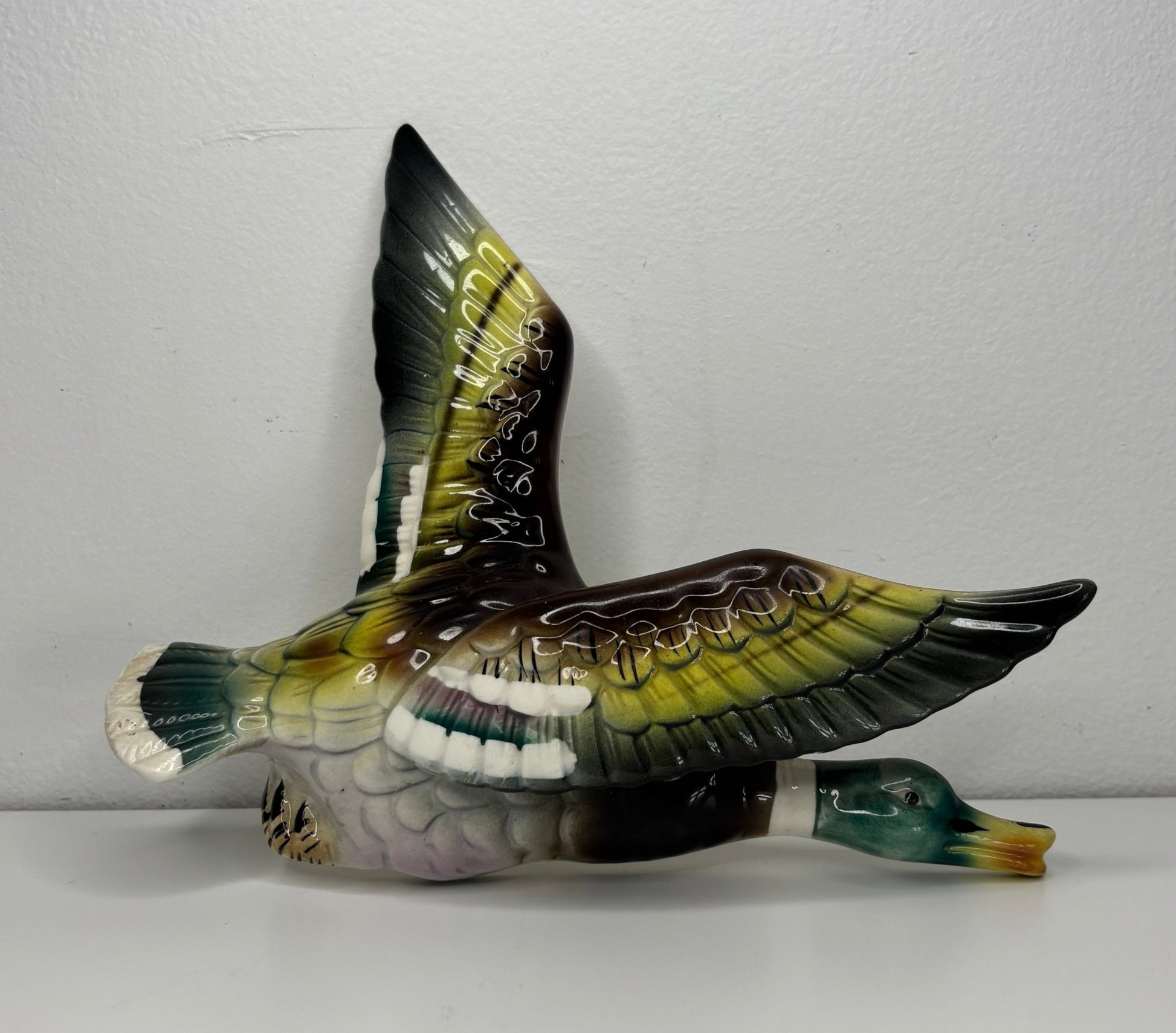 Decorative bird figurine with open wings on a white surface and light gray background