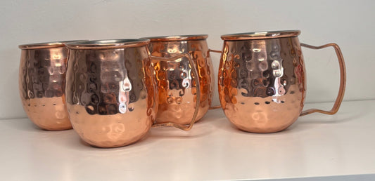 Set of four copper mugs with handles on a white surface