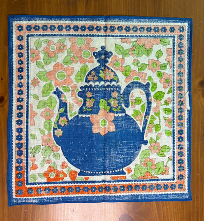 Decorative fabric square with a blue pitcher and floral design on a wooden surface
