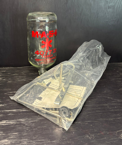 Clear plastic bag with vintage truck design on a dark surface, next to a glass bottle with 'Mack' branding.