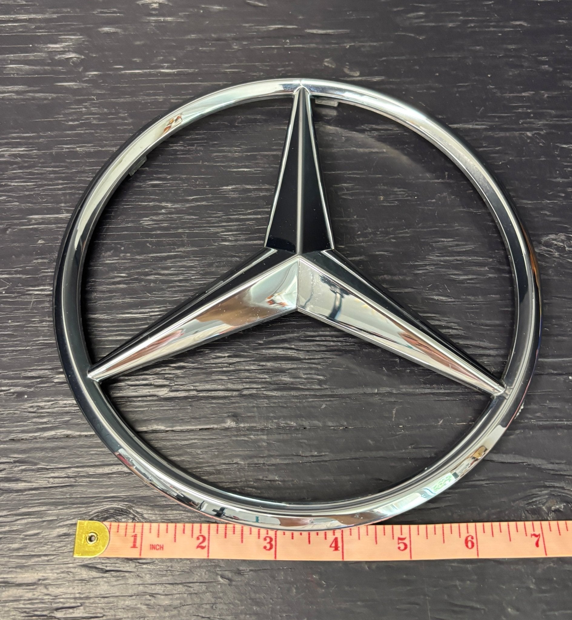 Mercedes-Benz logo on a dark surface with a ruler for scale.