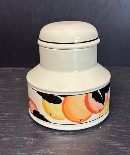 White ceramic jar with a lid and colorful fish design on a dark surface