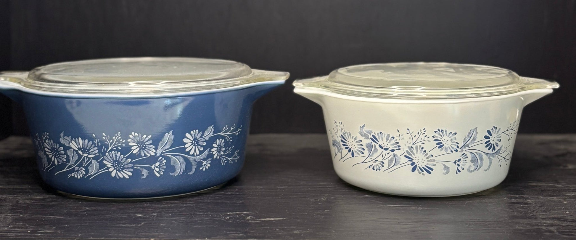 Two vintage-style ceramic cookware items with floral patterns on a dark surface.