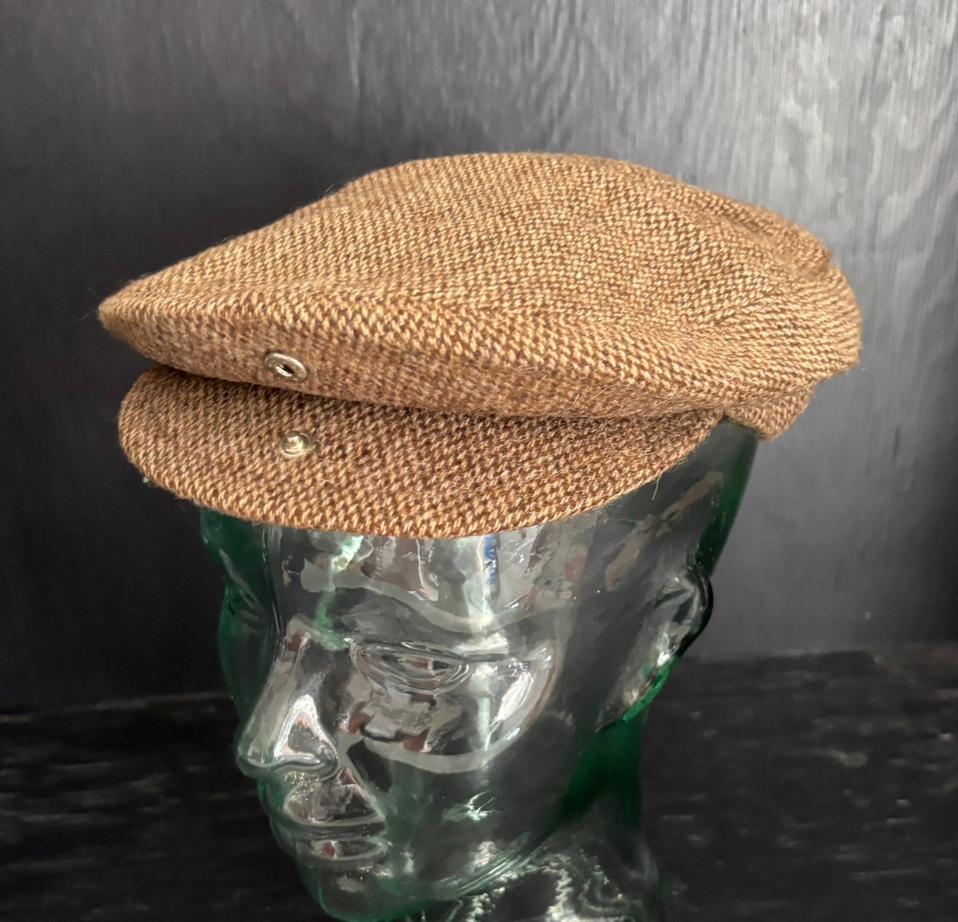 Brown tweed flat cap on a mannequin head against a dark background