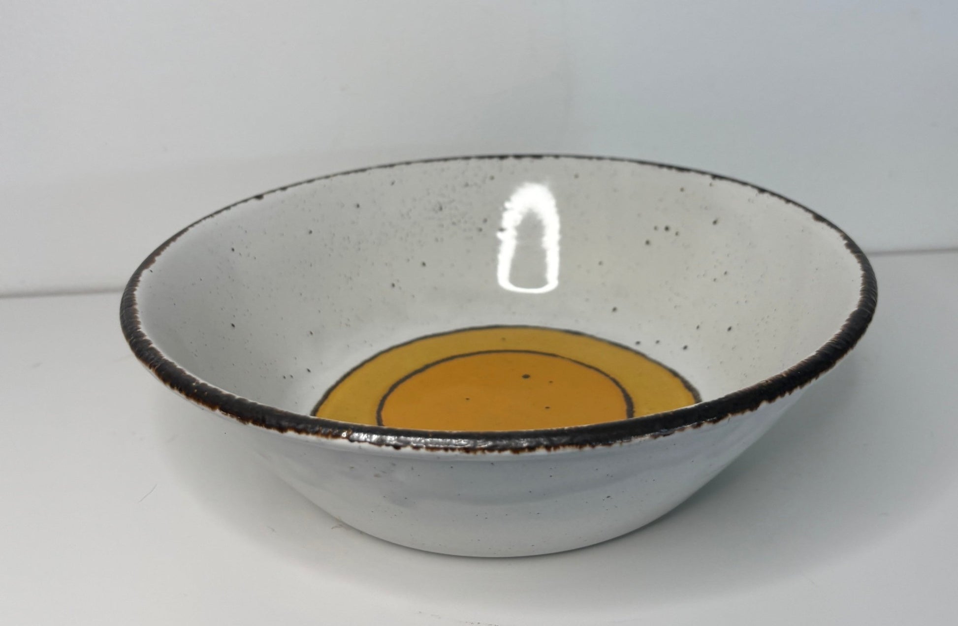 Ceramic bowl with a black rim and orange center on a white background